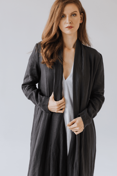 Woman wearing a long natural linen jacket with a minimalist design. Handmade and sustainably crafted, perfect for layering in all seasons.Woman wearing a long linen jacket in natural beige tone, standing in soft natural light.
 Sieviete valkā garu lina žaketi dabīgā bēšā tonī, stāvot maigā dienasgaismā.