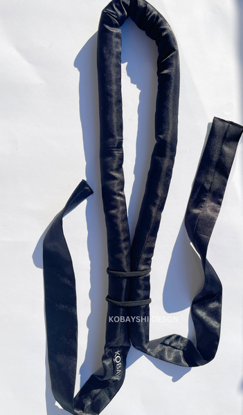A long black satin heatless hair curler ribbon with two folded parts and a brand name visible on the curler's end.