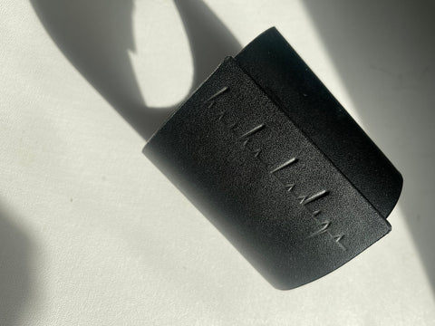 Melnas ādas aproces aproce ar reljefu logotipu un neredzamu magnēta atvērumu